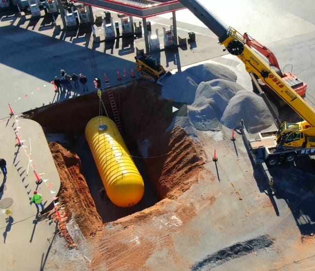 Large yellow underground storage tank being lowered into an excavated trench by a crane at a construction site. Large yellow underground storage tank being lowered into an excavated trench by a crane at a construction site.