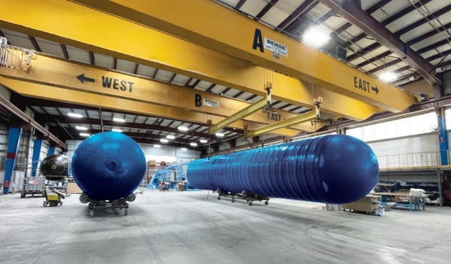 Large blue fiberglass storage tank being moved by overhead cranes inside an industrial manufacturing facility. Large blue fiberglass storage tank being moved by overhead cranes inside an industrial manufacturing facility.