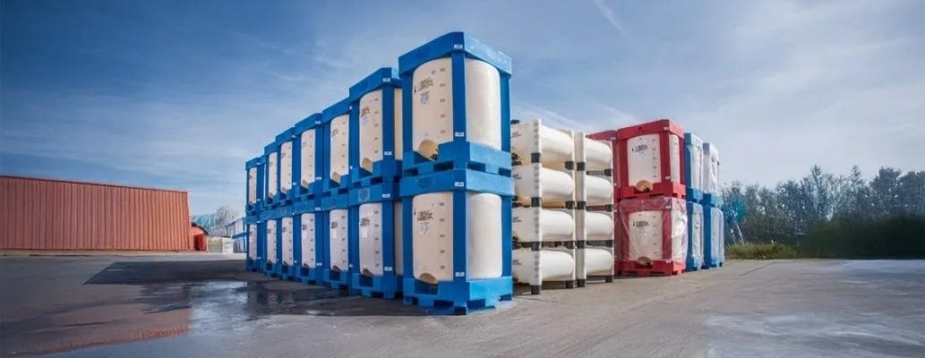Stacked IBC totes in protective blue, white, and red frames stored outdoors on an industrial lot for water or chemical transport. Stacked IBC totes in protective blue, white, and red frames stored outdoors on an industrial lot for water or chemical transport.