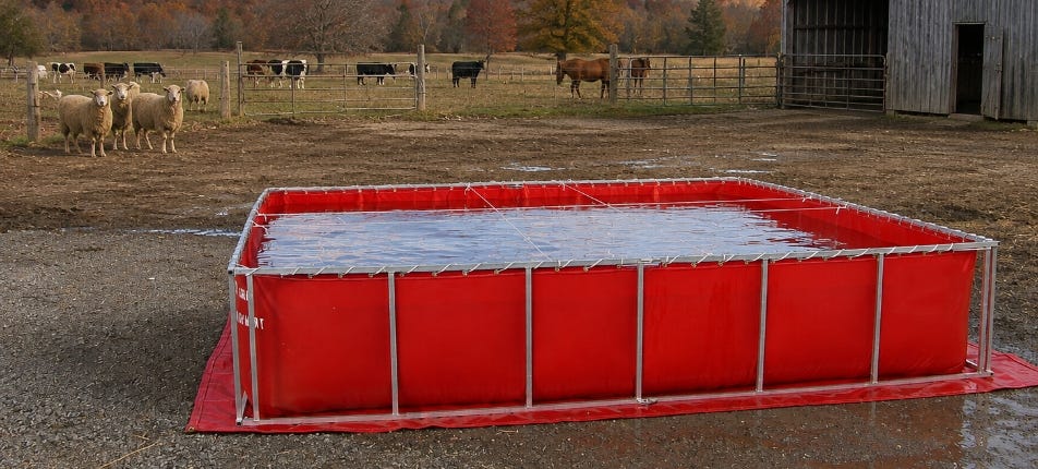 Red folding-frame portable water tank filled with water in a farmyard, with sheep, cattle, and a barn in the background. Red folding-frame portable water tank filled with water in a farmyard, with sheep, cattle, and a barn in the background.