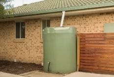 Green vertical water storage tank installed beside a residential home Green vertical water storage tank installed beside a residential home