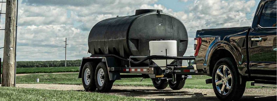 A pickup truck hauling a cone bottom tank for mixing farm chemicals alongside a black portable tank with surge control. A pickup truck hauling a cone bottom tank for mixing farm chemicals alongside a black portable tank with surge control.