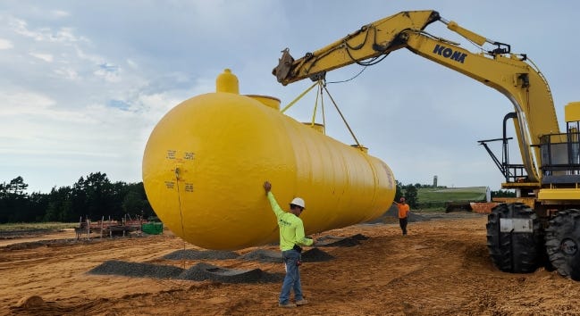 Large yellow underground stormwater tank being lowered into an excavation by an excavator as workers guide it into place. Large yellow underground stormwater tank being lowered into an excavation by an excavator as workers guide it into place.
