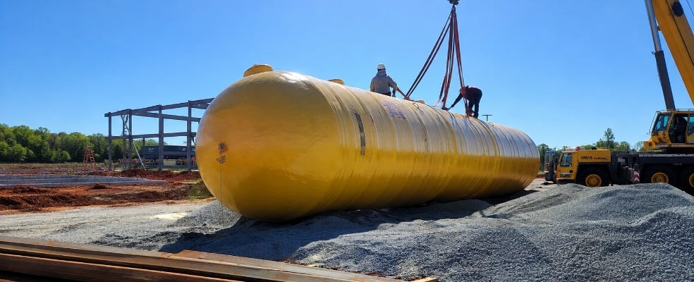 Large yellow underground storage tank being rigged by crane as workers prepare it for installation at a construction site. Large yellow underground storage tank being rigged by crane as workers prepare it for installation at a construction site.