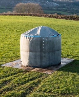 Dome-shaped water storage tank installed on a base in an open grassy field. Dome-shaped water storage tank installed on a base in an open grassy field.