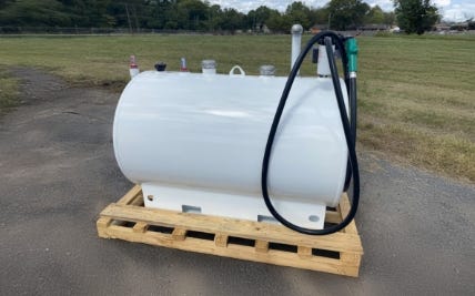White horizontal fuel storage tank with hose and dispensing nozzle mounted on a wooden pallet outdoors. White horizontal fuel storage tank with hose and dispensing nozzle mounted on a wooden pallet outdoors.