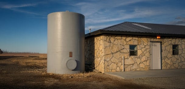 Tall fiberglass water storage tank installed beside a stone building in a dry rural landscape. Tall fiberglass water storage tank installed beside a stone building in a dry rural landscape.