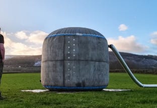 Large dome-shaped water storage tank installed in a grassy field with an inlet pipe attached. Large dome-shaped water storage tank installed in a grassy field with an inlet pipe attached.