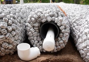 Close-up of EZflow drainage bundle with a pipe outlet and PVC fitting for foundation or French drain installation. Close-up of EZflow drainage bundle with a pipe outlet and PVC fitting for foundation or French drain installation.