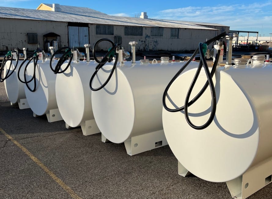 Row of white horizontal fuel and oil storage tanks with attached hoses and fittings lined up outdoors at an industrial facility. Row of white horizontal fuel and oil storage tanks with attached hoses and fittings lined up outdoors at an industrial facility.