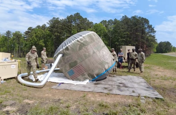 Inflatable concrete Omni Tank being inflated on an Instaslab foundation mat during a field installation demonstration with military personnel nearby. Inflatable concrete Omni Tank being inflated on an Instaslab foundation mat during a field installation demonstration with military personnel nearby.