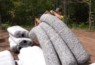 Worker carrying lightweight EZflow drainfield bundles by hand at an outdoor septic installation site. Worker carrying lightweight EZflow drainfield bundles by hand at an outdoor septic installation site.