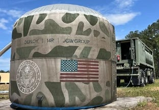 Camouflage-pattern Deploy 14R flexible concrete tank with U.S. flag graphic, set up in a field beside a military transport truck. Camouflage-pattern Deploy 14R flexible concrete tank with U.S. flag graphic, set up in a field beside a military transport truck.
