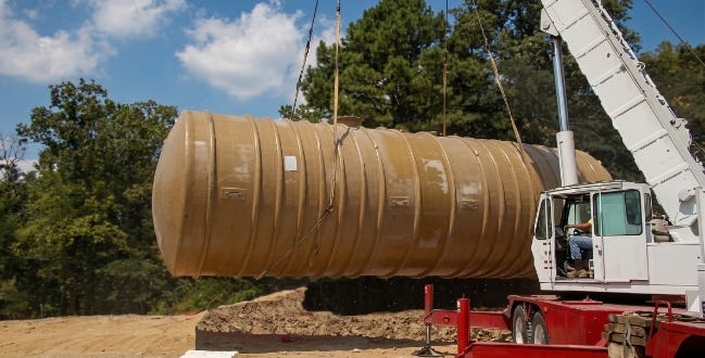 Large fiberglass underground storage tank being lifted by a crane for installation at a construction site. Large fiberglass underground storage tank being lifted by a crane for installation at a construction site.