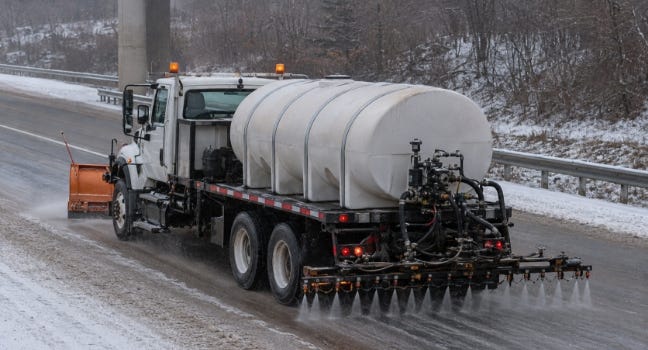 Snowplow truck spraying brine on a winter road from white polyethylene tanks mounted on the flatbed. Snowplow truck spraying brine on a winter road from white polyethylene tanks mounted on the flatbed.
