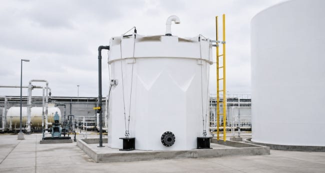 White brine storage tank with piping, tie-downs, and a yellow access ladder installed on a concrete pad at an industrial facility. White brine storage tank with piping, tie-downs, and a yellow access ladder installed on a concrete pad at an industrial facility.