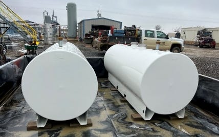 Two white horizontal bulk steel storage tanks positioned outdoors at an industrial equipment yard. Two white horizontal bulk steel storage tanks positioned outdoors at an industrial equipment yard.