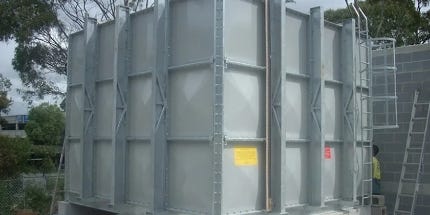 Large modular fiberglass storage tank with metal support frame, ladder, and access platform installed at an industrial site. Large modular fiberglass storage tank with metal support frame, ladder, and access platform installed at an industrial site.