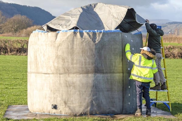 Workers using a ladder to finish installing the top cover on a deployed inflatable concrete Omni Tank in an open field. Workers using a ladder to finish installing the top cover on a deployed inflatable concrete Omni Tank in an open field.