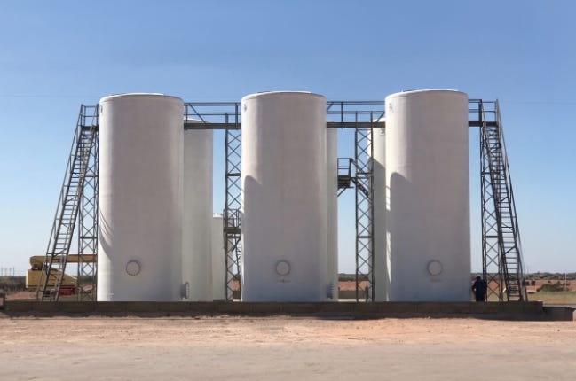 Three large white fiberglass industrial storage tanks with access stairs and elevated platforms installed at an outdoor facility. Three large white fiberglass industrial storage tanks with access stairs and elevated platforms installed at an outdoor facility.