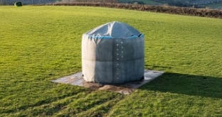 Dome-shaped water storage tank installed on a base in an open grassy field. Dome-shaped water storage tank installed on a base in an open grassy field.