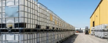 Stacked caged IBC totes stored in an outdoor yard and transported on a trailer behind a pickup truck. Stacked caged IBC totes stored in an outdoor yard and transported on a trailer behind a pickup truck.