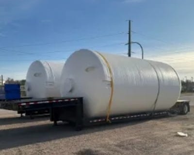Two white fiberglass storage tanks secured on a flatbed trailer for transport. Two white fiberglass storage tanks secured on a flatbed trailer for transport.