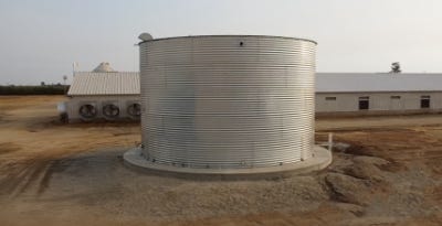 Large corrugated steel rainwater storage tank installed on a concrete pad at a rural agricultural site. Large corrugated steel rainwater storage tank installed on a concrete pad at a rural agricultural site.