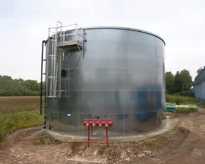 Large stainless steel storage tank with access ladder, platform, and red piping installed outdoors near a field. Large stainless steel storage tank with access ladder, platform, and red piping installed outdoors near a field.