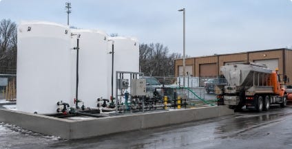 White brine storage tanks with pumping equipment installed on a containment pad beside a maintenance facility and service truck. White brine storage tanks with pumping equipment installed on a containment pad beside a maintenance facility and service truck.