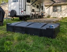 Black above-ground septic tank installed on grass beside an RV trailer in a residential outdoor setting. Black above-ground septic tank installed on grass beside an RV trailer in a residential outdoor setting.